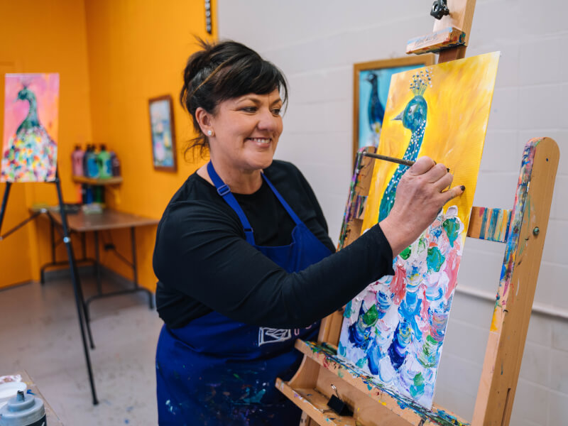 A woman learns how to paint a colourful peacock.